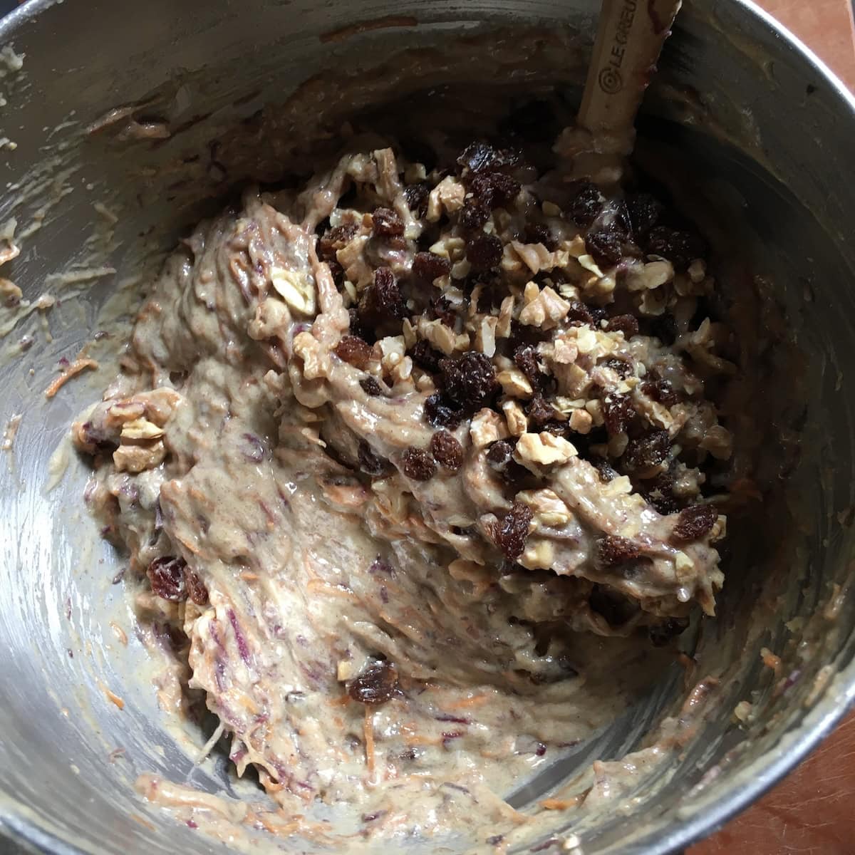 Toasted walnuts and  raisins being folded into the purple carrot cake batter for a classic homemade carrot cake with walnuts.