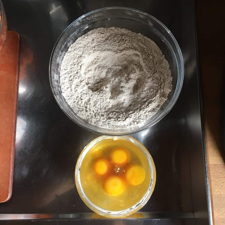 A bowl of whisked dry ingredients and a separate bowl of cracked eggs with vanilla extract about to be added to the wet ingredients for carrot cake batter.