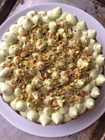 A double layer no-raisin best carrot cake with pecans and matcha cream cheese frosting, piped in kisses and garnished with toasted pistachios.