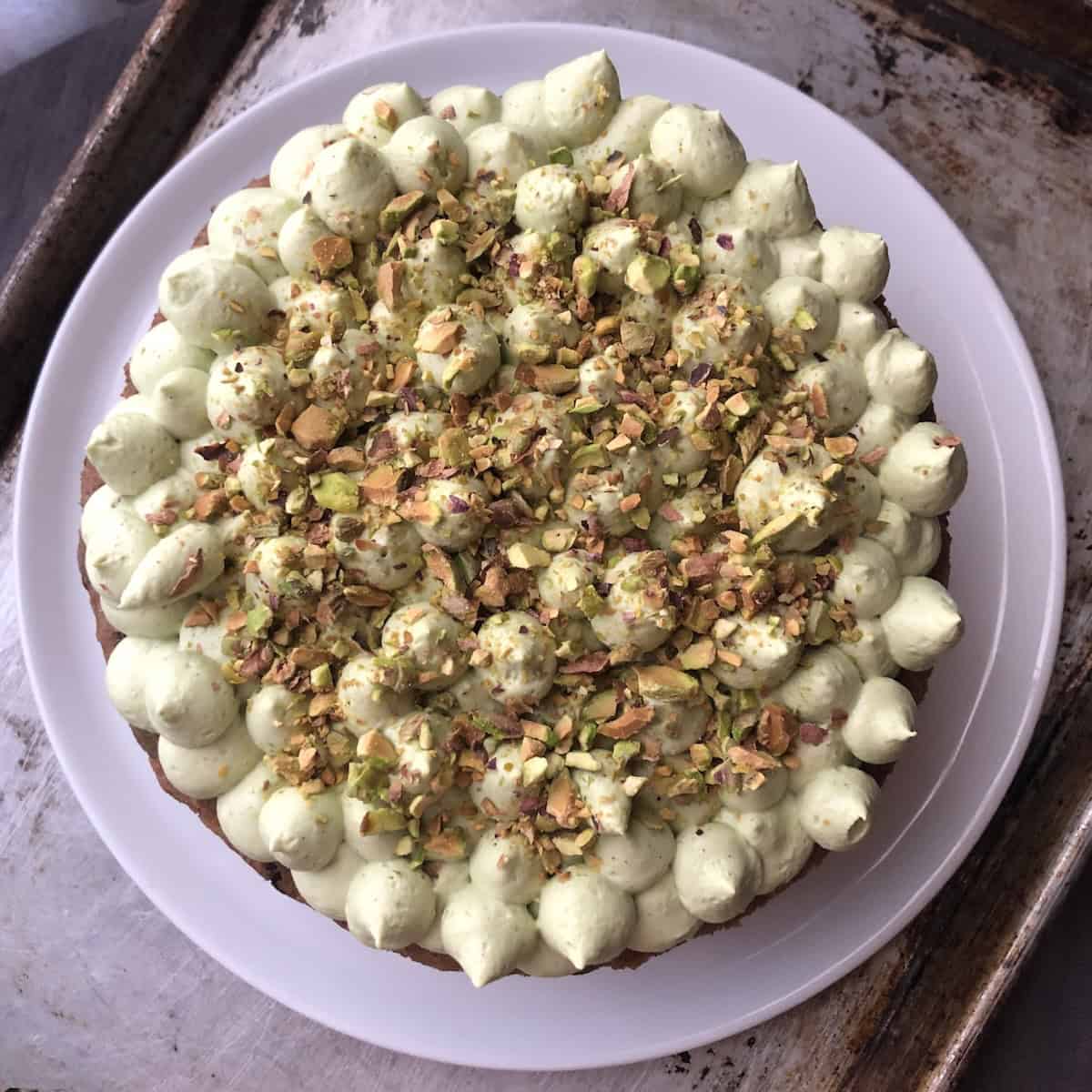 A double layer no-raisin carrot cake with pecans and matcha cream cheese frosting, piped in kisses and garnished with toasted pistachios.