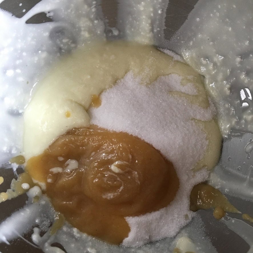 A stand mixer bowl with creamed butter and oil, mixture with sugar, and applesauce just added before combining the wet ingredients for a simple homemade carrot cake recipe from scratch.