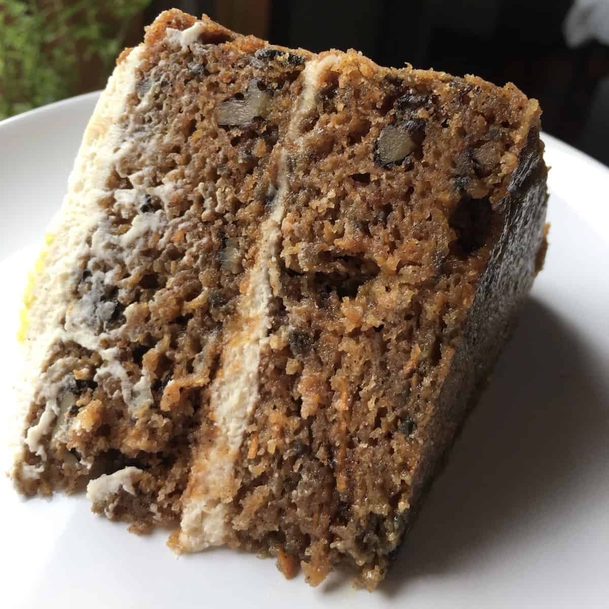 A slice of classic carrot cake with cream cheese icing with vanilla beans, toasted walnuts, raisins, and a deeply, visibly moist crumb.