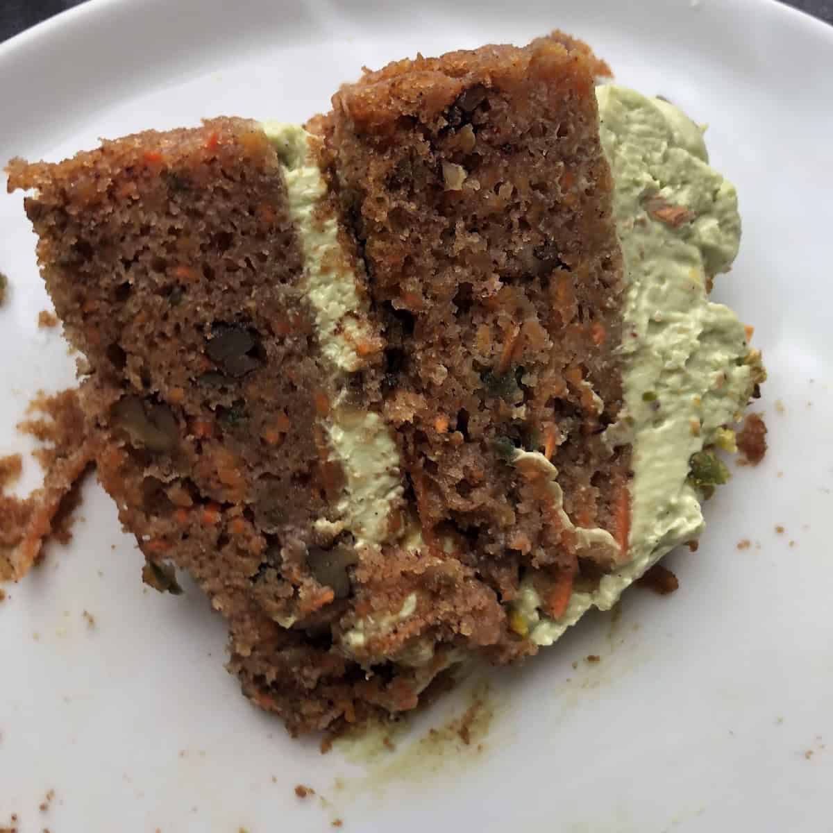 A slice of orange carrot cake with toasted pecans, no raisins, and spring-green matcha cream cheese mascarpone frosting showing a beautifully moist crumb.