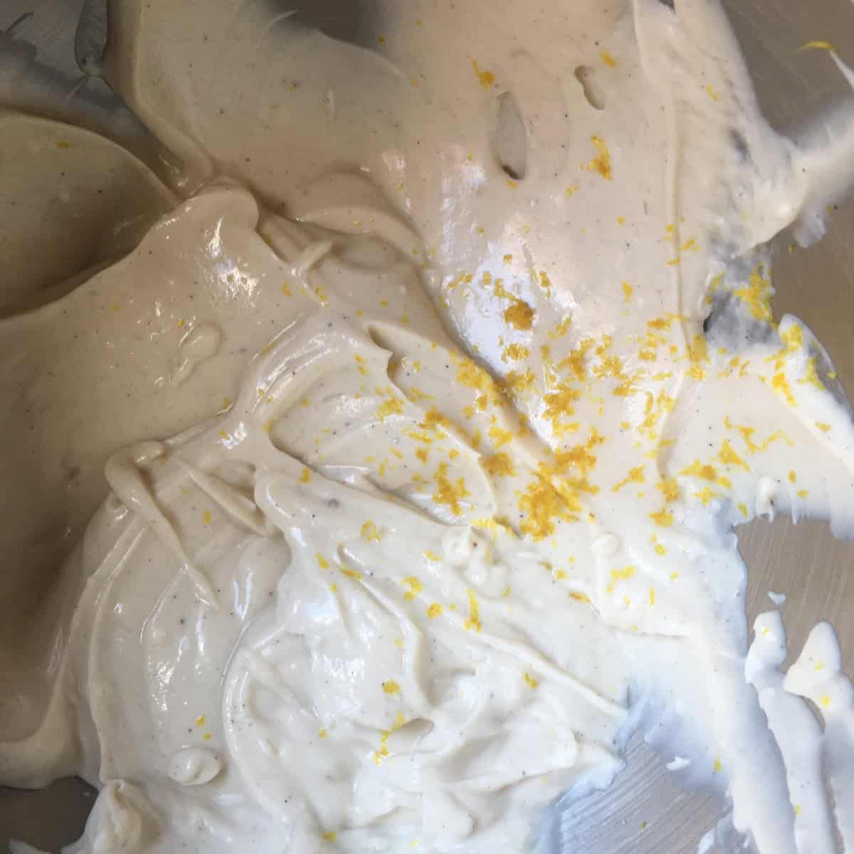 A bowl of homemade cream cheese frosting with vanilla bean seeds and lemon zest looking light for a fluffy carrot cake icing that keeps well and can be frozen ahead of time.