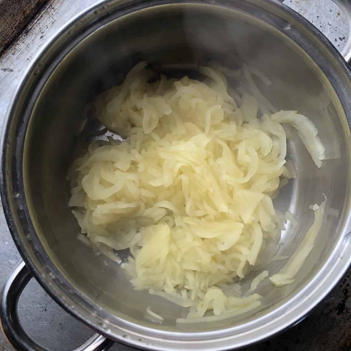 Completely soft cooked apples with a splash of water added, ready to mash into smooth homemade applesauce for a healthy carrot cake recipe made from scratch.