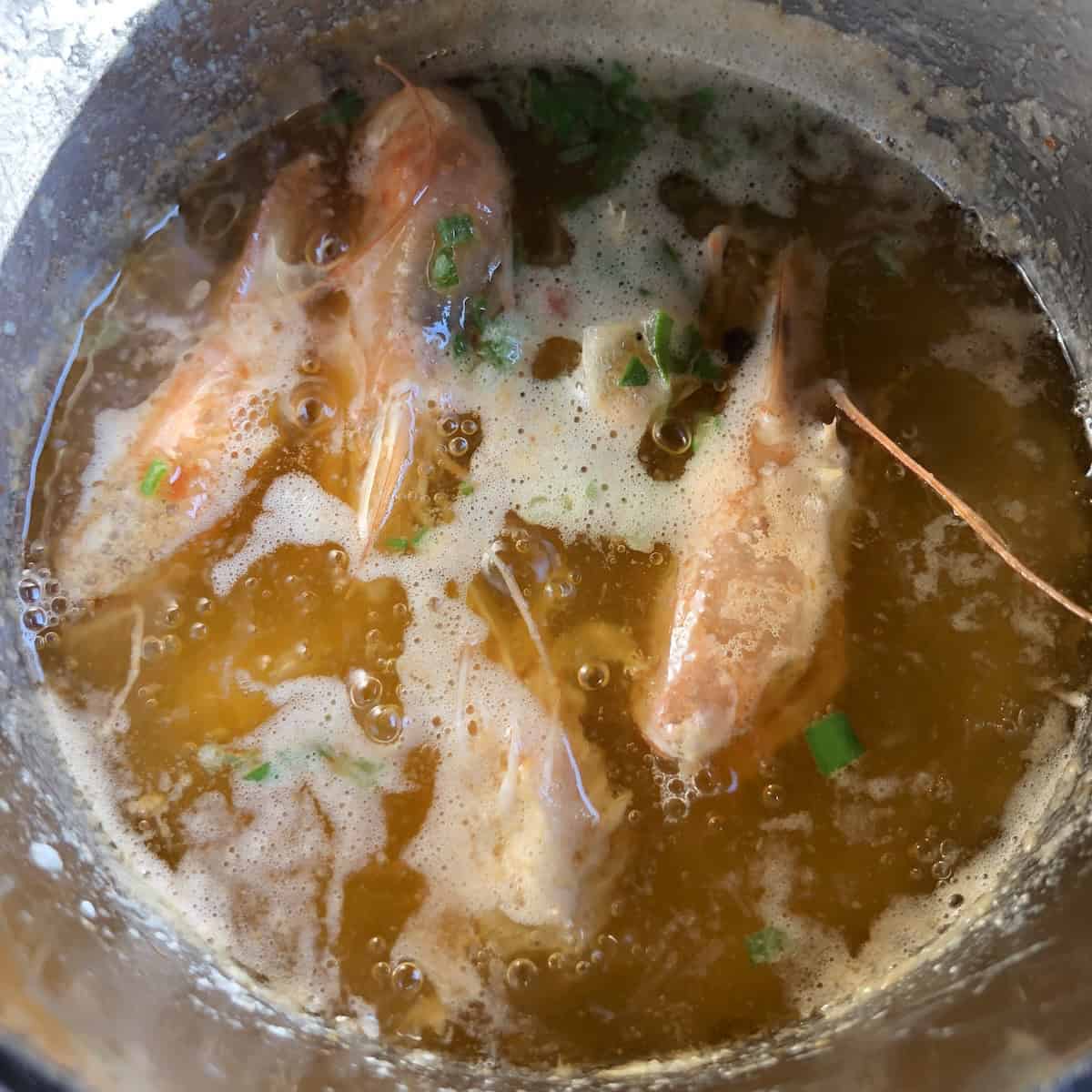 A small pot filled with clarified butter with raw shrimp heads and scallions added to make shrimp butter for shrimp rolls, shrimp pasta, shrimp gratin, shrimp garlic butter, and more.