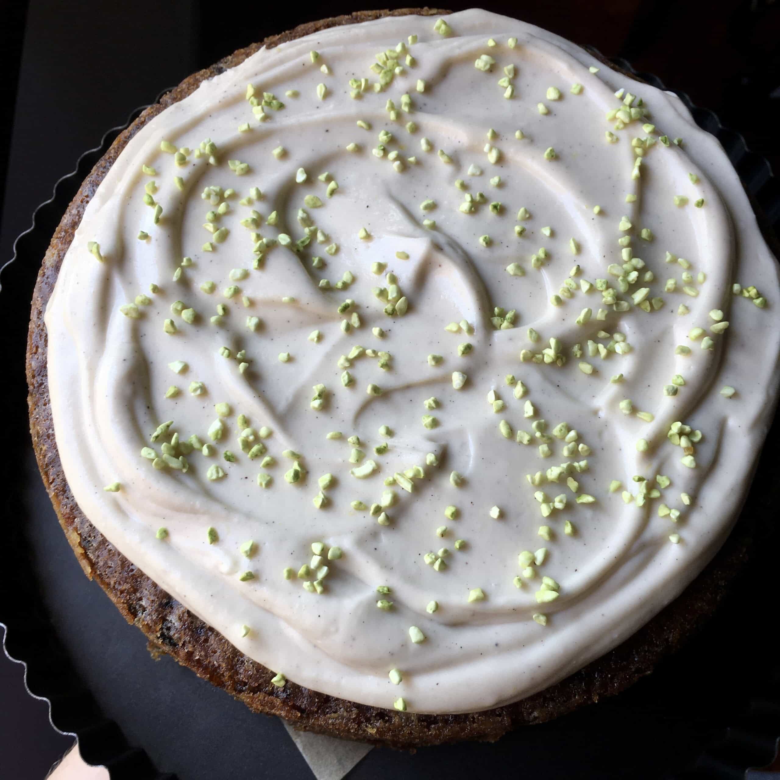 A frosted purple carrot cake with vanilla bean cream cheese frosting and pale green freeze-dried pistachio garnish, a stunning homemade carrot cake for Easter or any celebration.