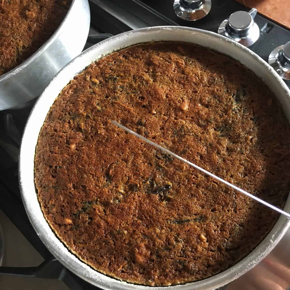 A clean cake tester pulled from the center of a carrot cake with no batter clinging to it, showing exactly when a carrot cake recipe is perfectly done.