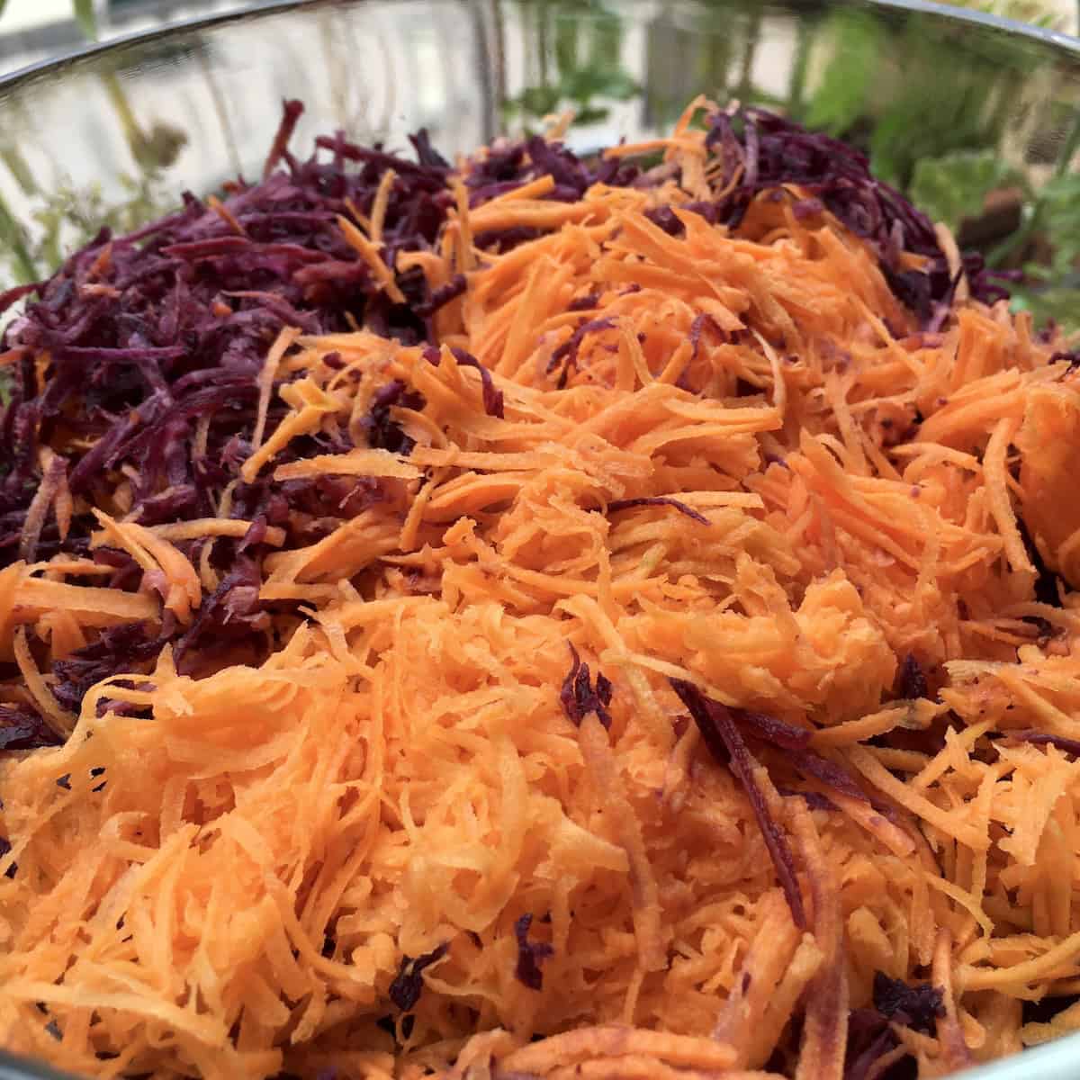 A bowl of finely grated purple and orange carrots for carrot cake - freshly grated carrots that mostly disappear into the carrot cake batter and are never chewy.