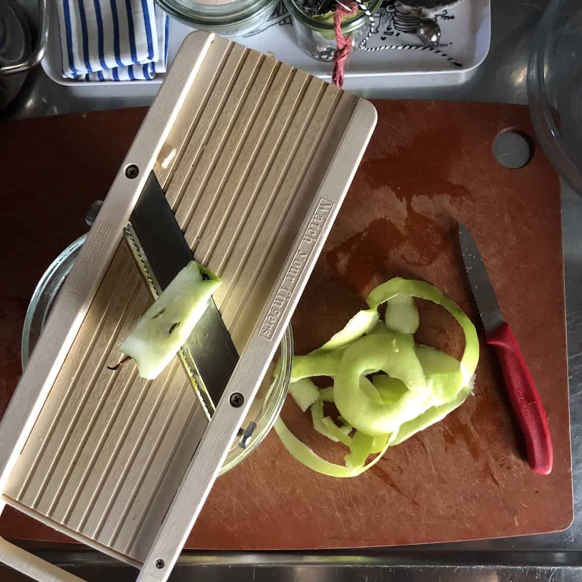A peeled apple being finely julienned on a mandoline to make homemade applesauce showing the easy from-scratch method for a healthier carrot cake with applesauce instead of all the oil called for.