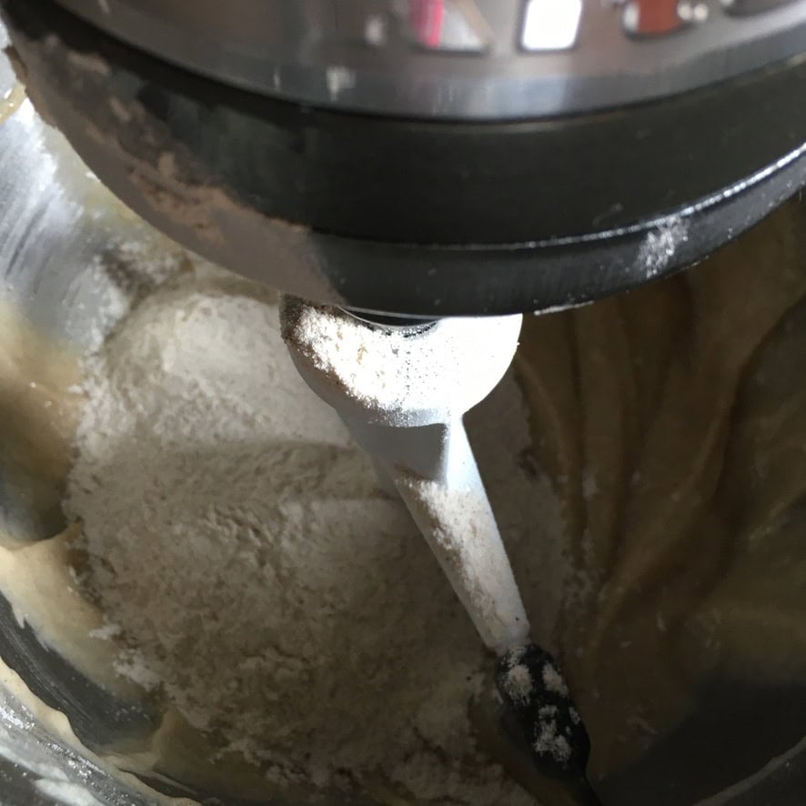 Half the flour mixture added to the butter, oil, sugar, and applesauce in a stand mixer bowl, a key step in making a moist carrot cake recipe from scratch.
