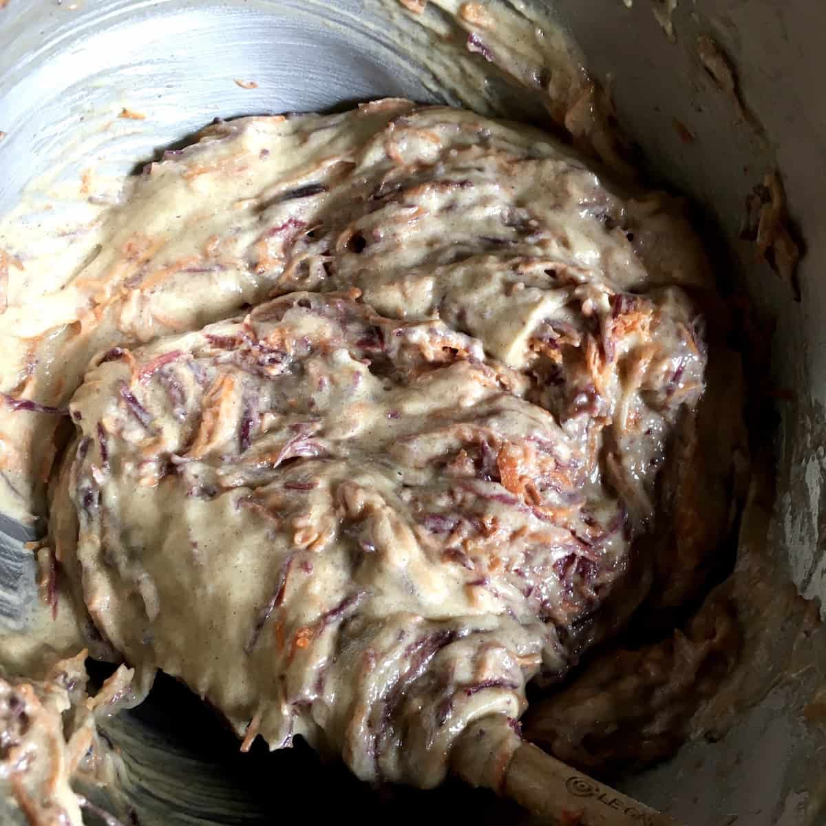 Folding freshly shredded carrots into the carrot cake batter before the optional toasted nuts and raisins are added.
