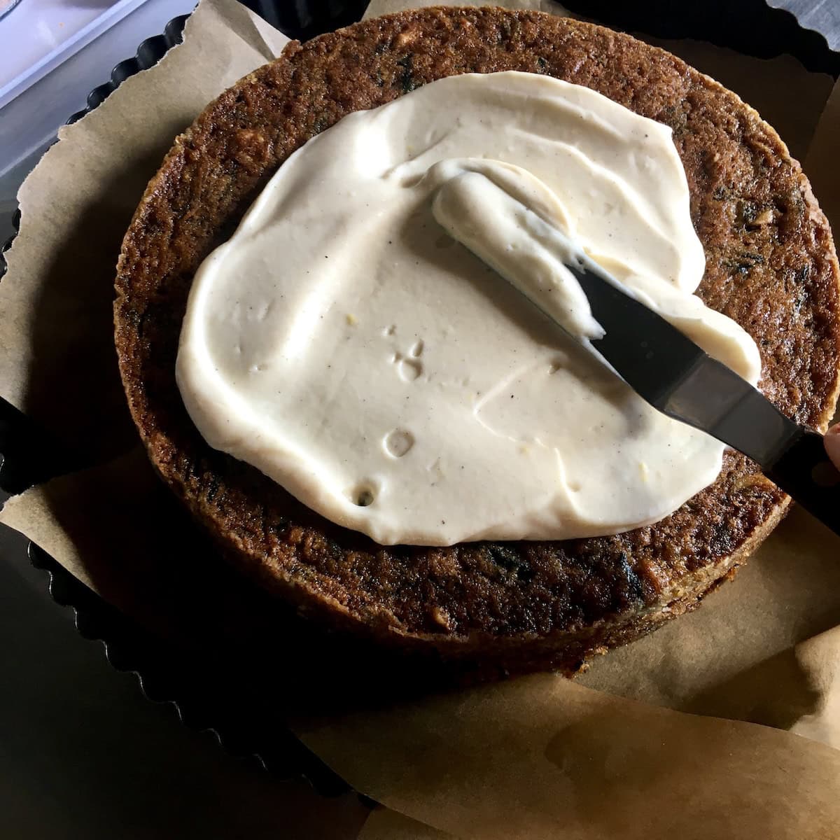 An offset spatula spreading cream cheese frosting on the bottom layer of a homemade purple carrot cake, showing how to frost a double layer carrot cake once fully cooled.