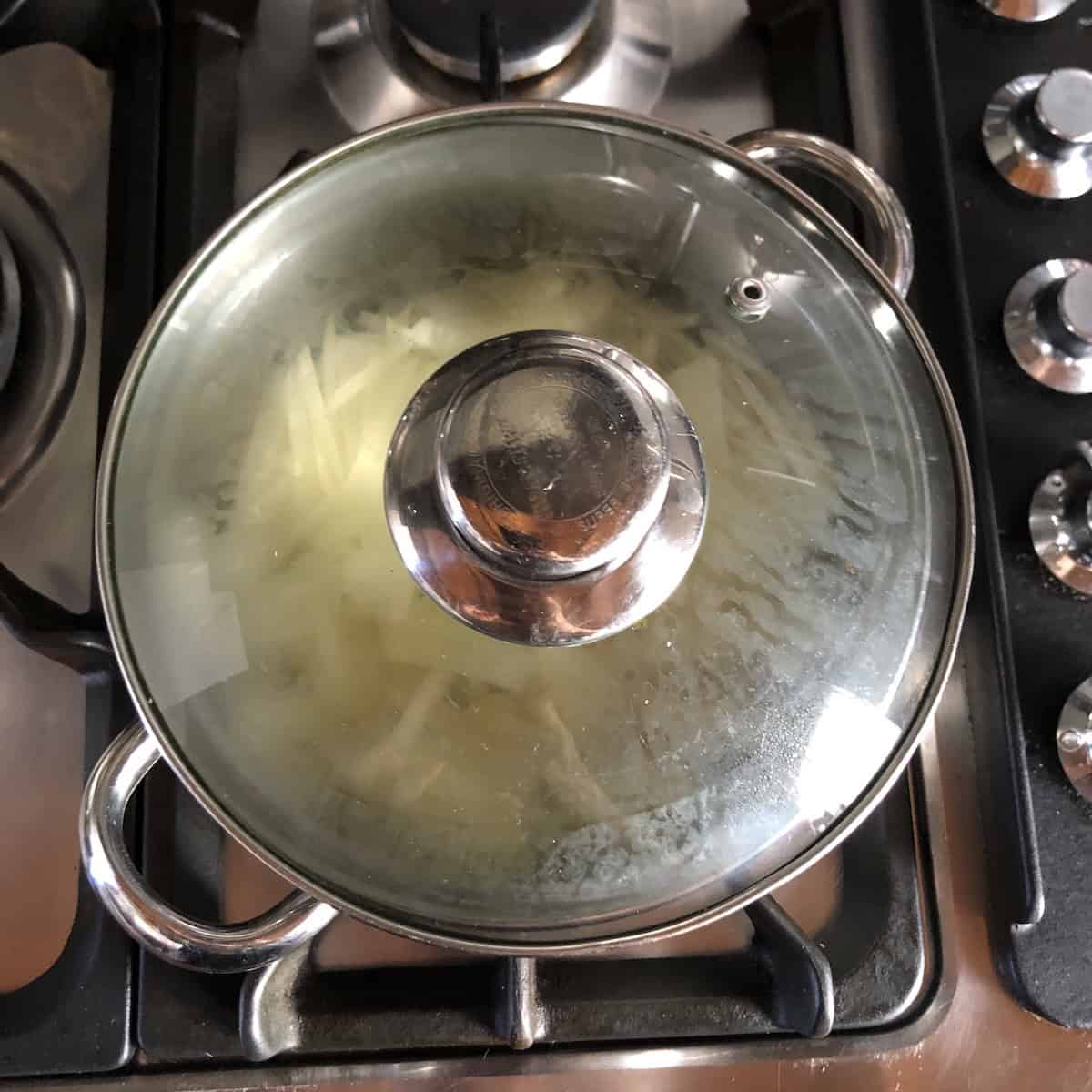 A covered pot of julienned apples simmering with water until tender for the first step to cooking an easy applesauce for a moist carrot cake from scratch.