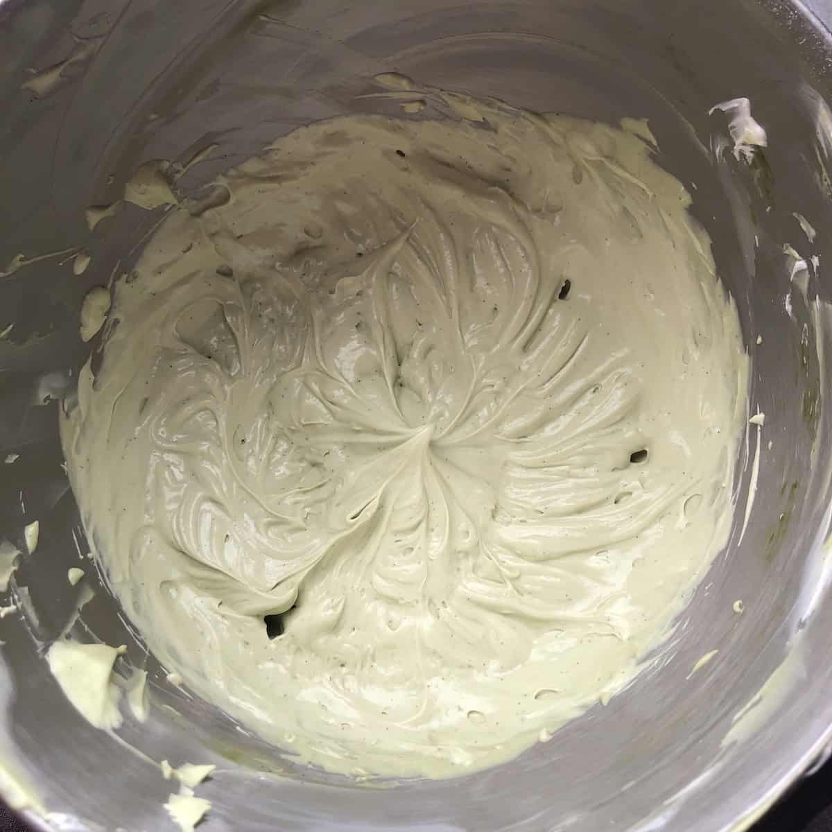 A mixing bowl filled with pale spring-green matcha cream cheese mascarpone frosting, ready to frost a carrot cake recipe for Easter or Mother's Day.
