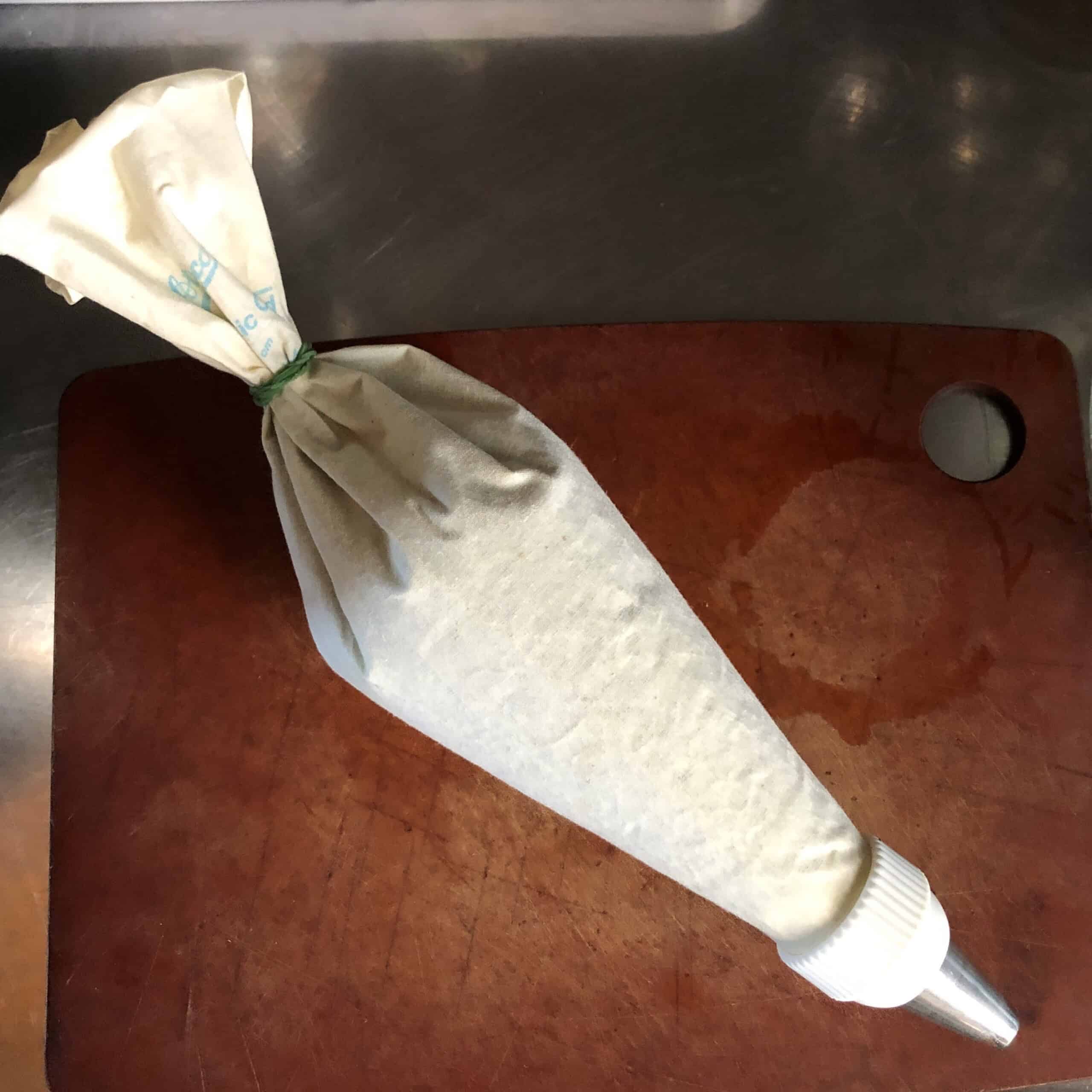 A piping bag fitted with a large round tip and filled with matcha cream cheese mascarpone frosting, tied and ready to pipe onto carrot cake.