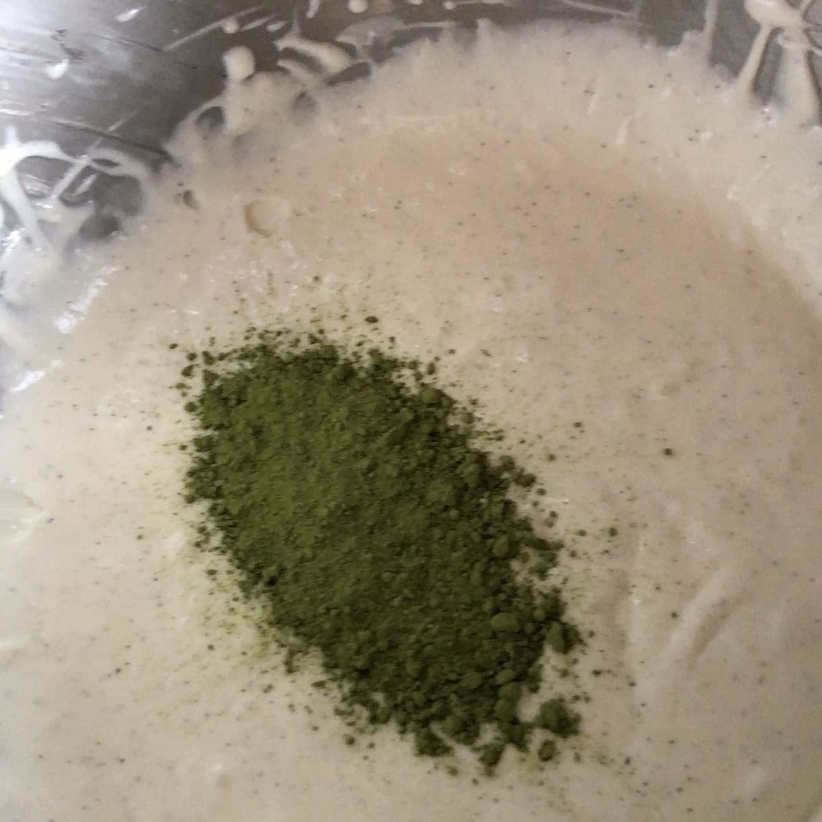 Matcha powder added to vanilla bean cream cheese mascarpone frosting in a stand mixer bowl before being incorporated, a stunning matcha recipe variation for carrot cake frosting.
