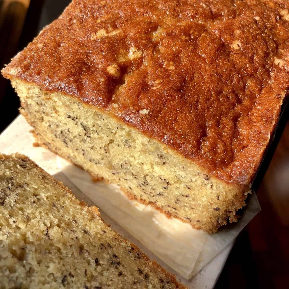 Closeup of a slice of moist banana bread on a pink marble tray showing a tender crumb so moist it looks like banana cake, easy banana bread recipe from scratch.
