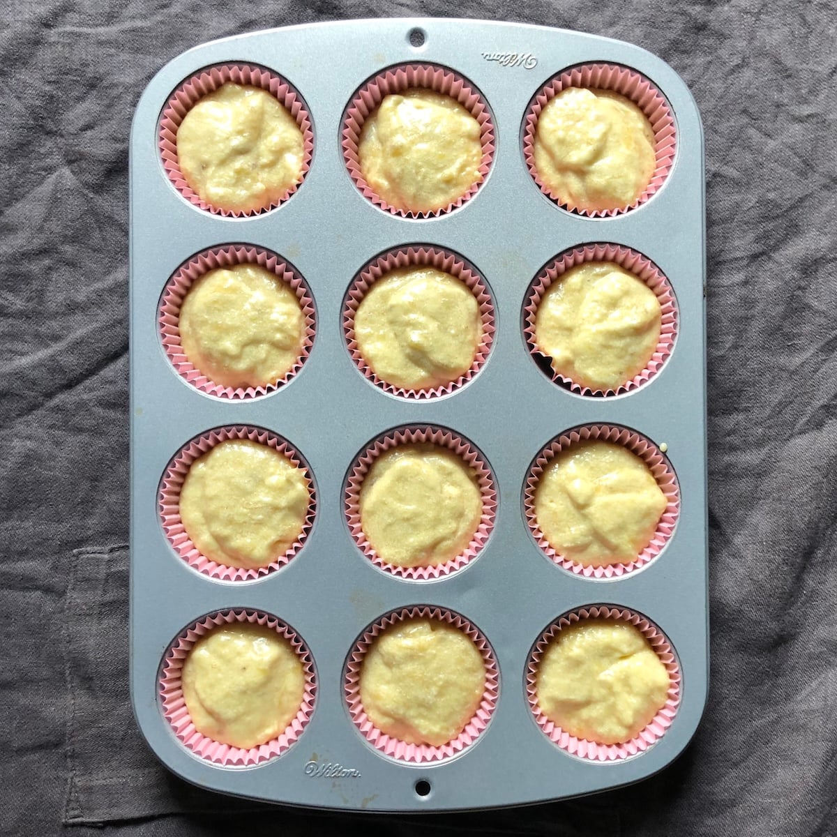12 muffin baking pan lined with pink paper liners and filled with pumpkin spice banana bread batter.