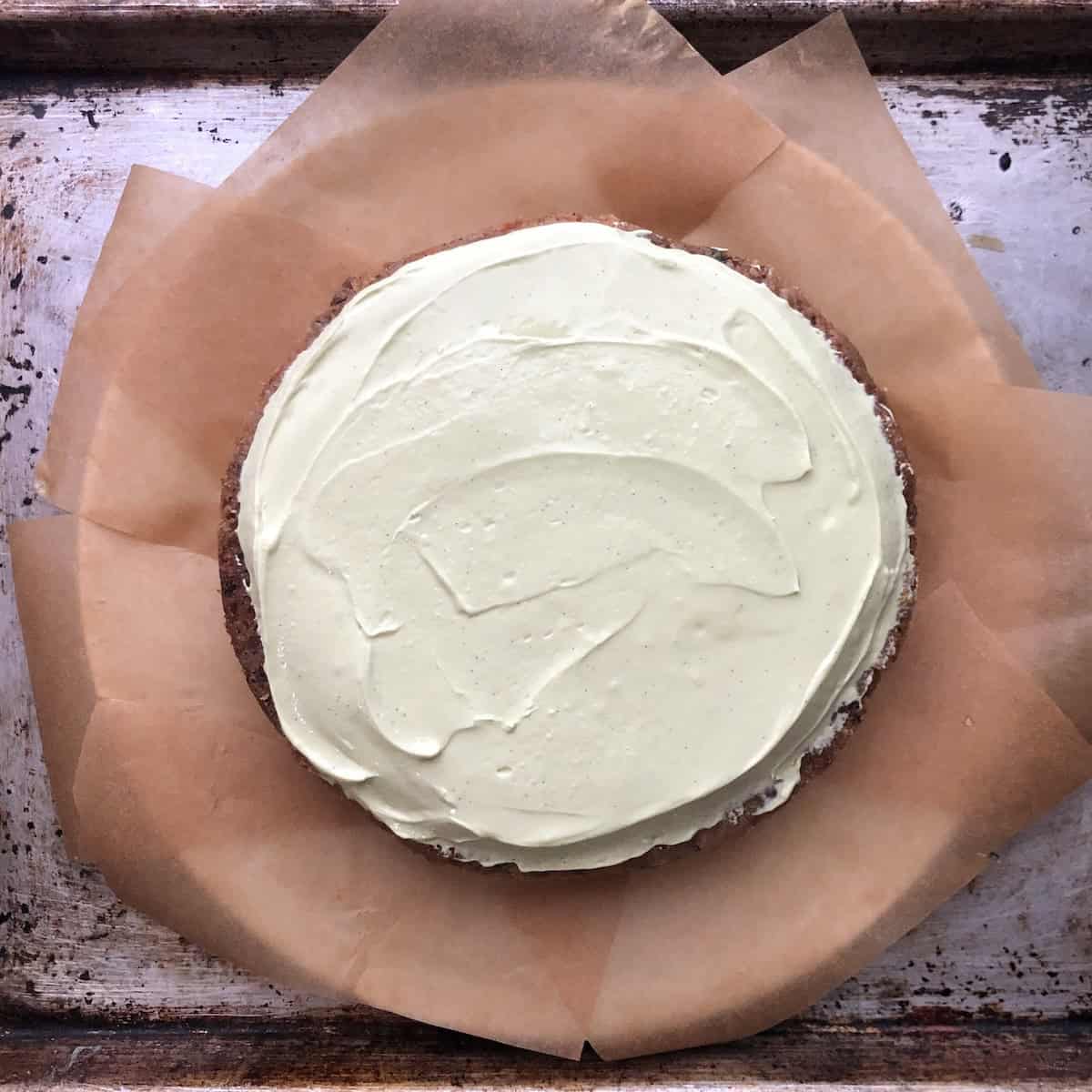 Bottom layer of easy carrot cake recipe with pecans and orange carrots, no raisins, frosted with pale green matcha cream cheese mascarpone frosting perfect for Easter.