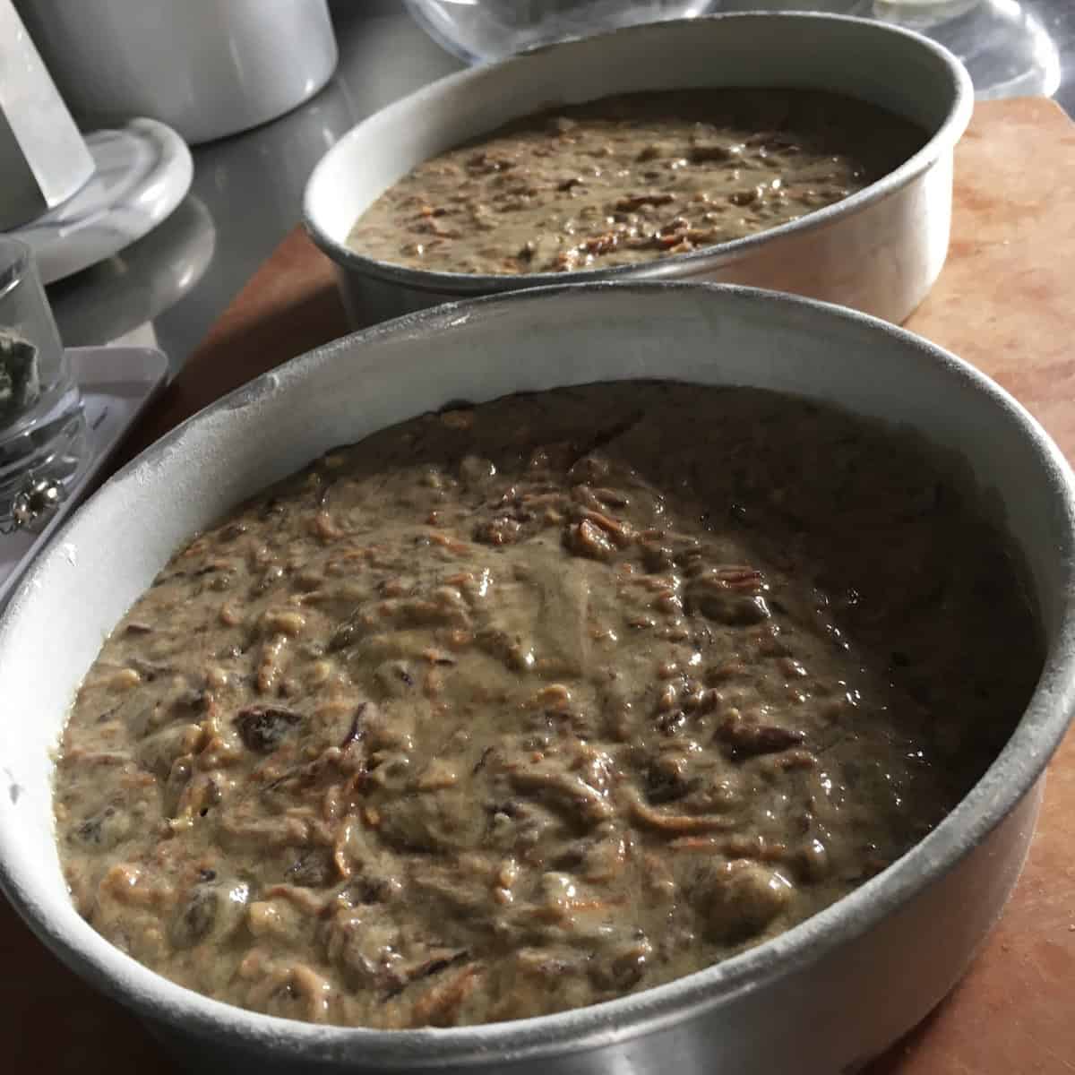 Purple carrot cake batter with toasted walnuts and raisins divided into two prepped 8-inch cake pans and ready to bake.