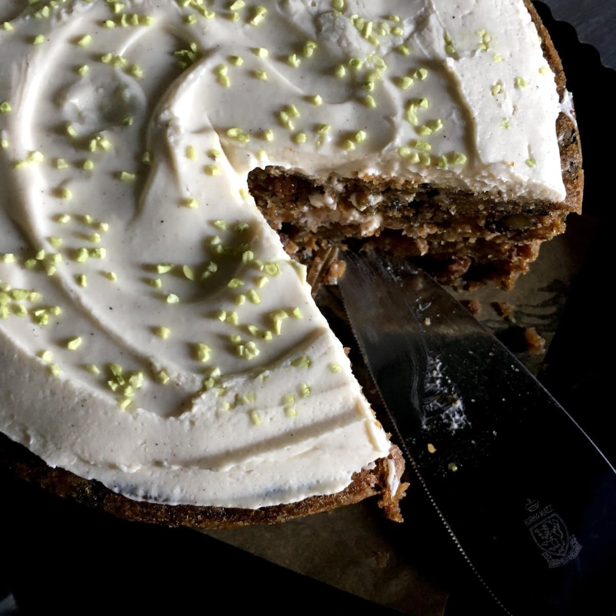 A purple carrot cake with a slice removed revealing a deeply moist crumb with walnuts and raisins. Does carrot cake have raisins? This classic version does, and you can make it days in advance.