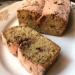 Sliced strawberry banana bread on a plate dusted with powdered strawberry sugar showing the moist crumb with freeze-dried strawberry pieces throughout.