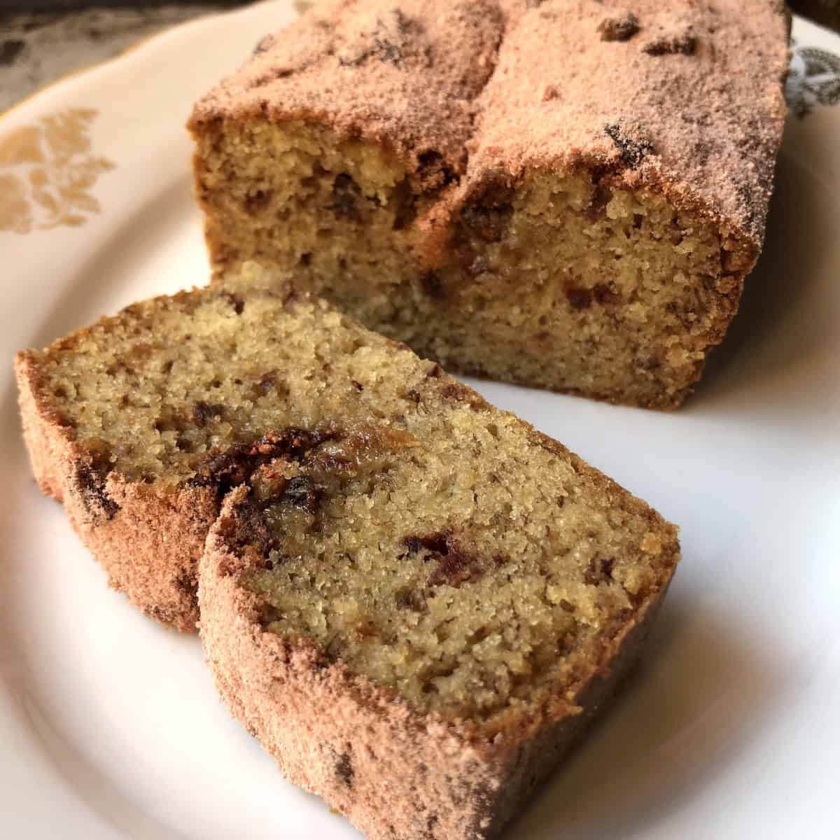 Sliced strawberry banana bread on a plate dusted with powdered strawberry sugar showing the moist crumb with freeze-dried strawberry pieces throughout.
