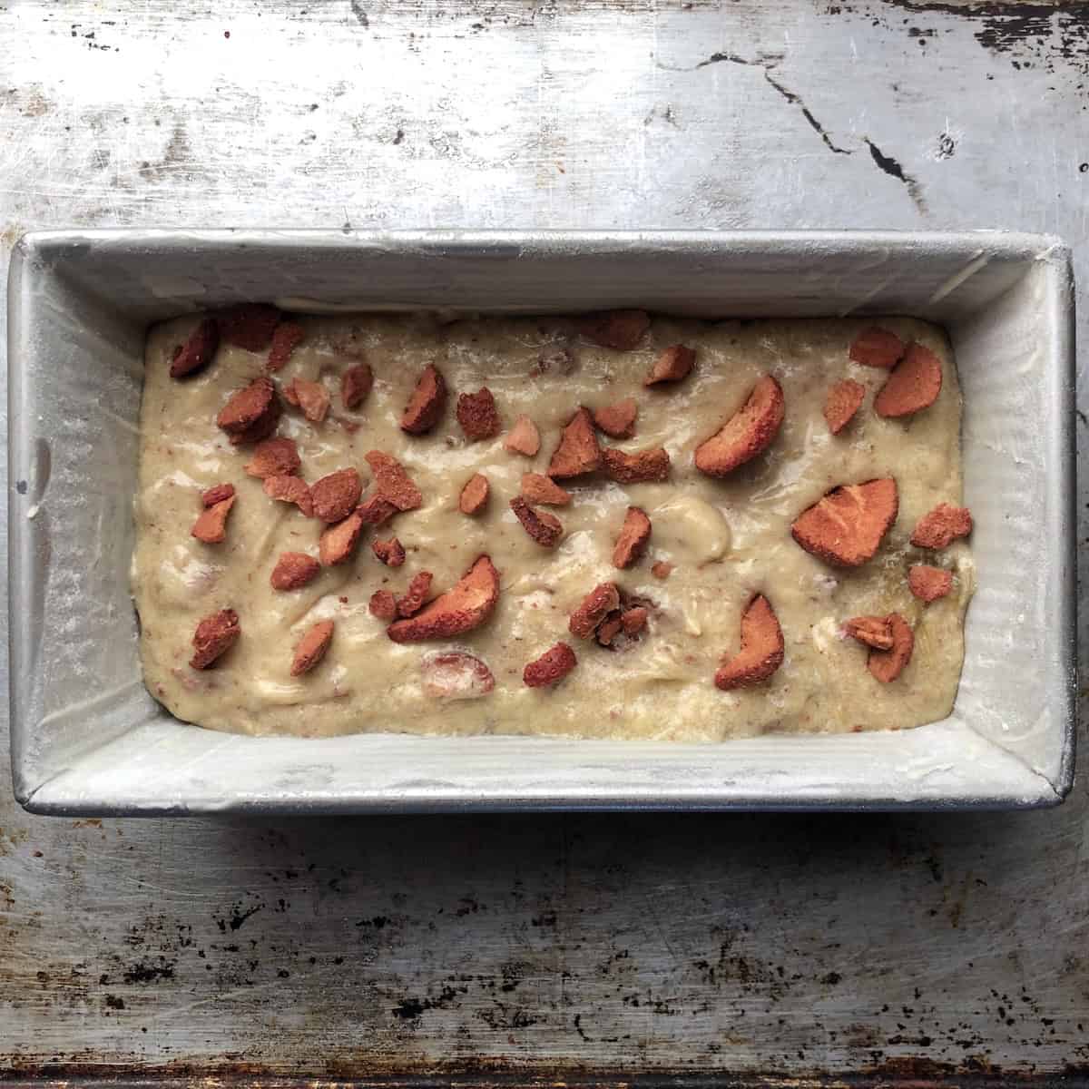Strawberry banana bread batter in a prepared loaf pan topped with freeze-dried strawberry pieces ready to bake.
