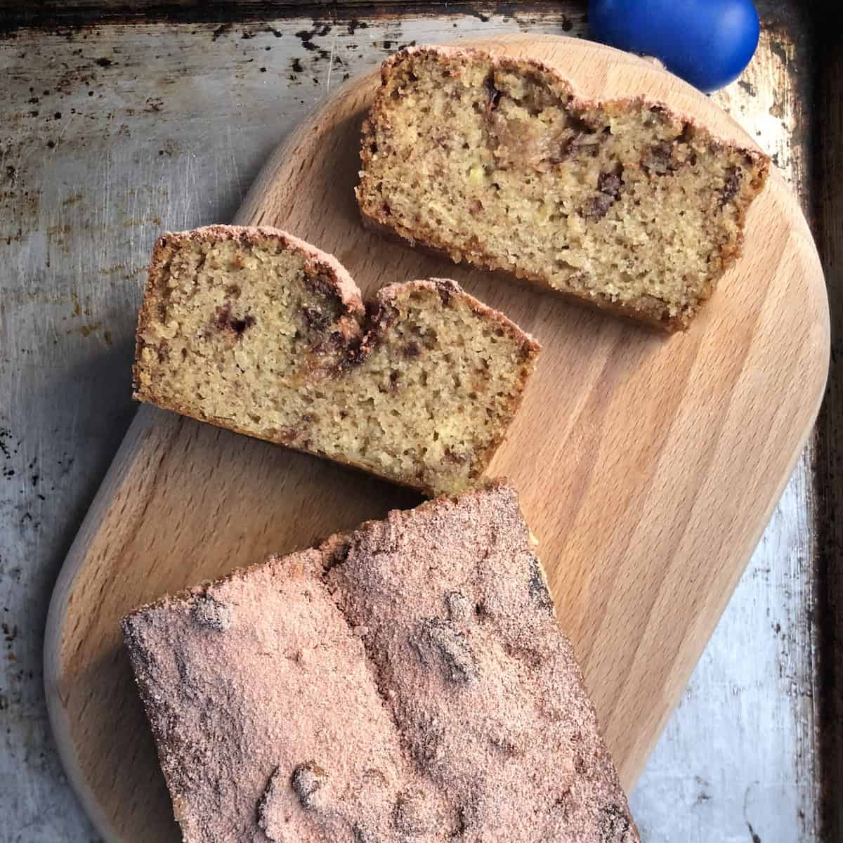 Sliced strawberry banana bread on a wooden cutting board with the loaf dusted in pink strawberry sugar and two slices showing the moist crumb.
