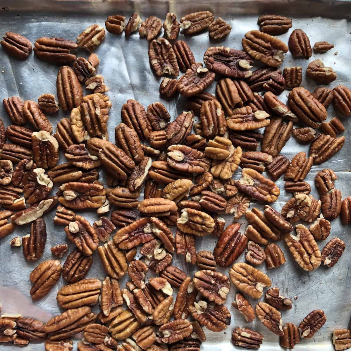 Toasted pecan halves on a sheet pan for carrot cake, golden and fragrant straight from the oven, ready to cool and be chopped.
