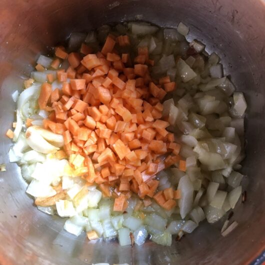 raw carrots added to a pot with EVOO, smashed garlic clove, and onions to cook