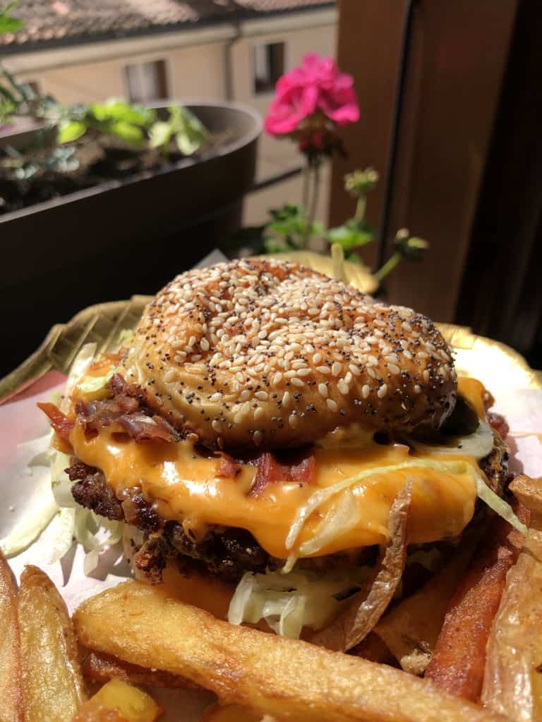 Beyond Burger looking beautifully beefy and cheesy on a platter with twice-fried french fries with a view of a pink gardenia in the background and view out of the window