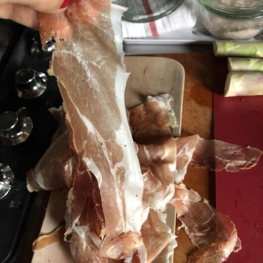 holding up a piece of speck to show the fat that can be trimmed off the sides and sauteed