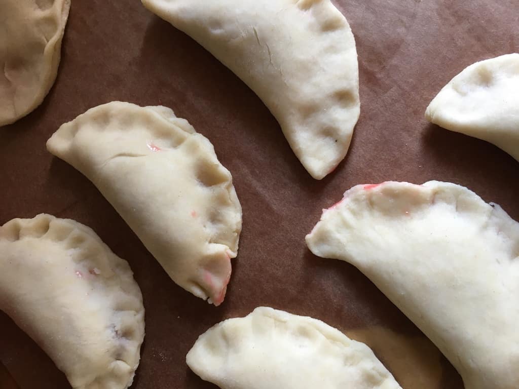 uncooked fried pies on brown parchment paper in the half-moon shape with the edges closed but not crimped with a fork yet