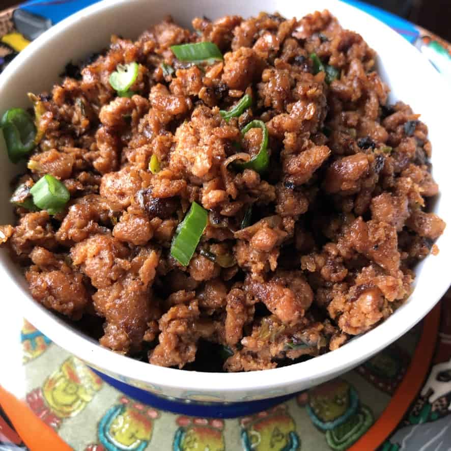 A bowl full of vegetarian beef taco meat in a bowl flecked with freshly sliced scallions.