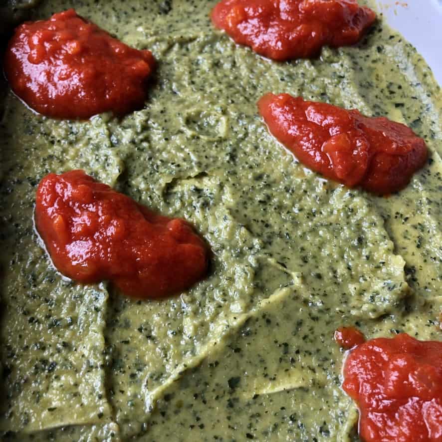 closeup of deep green zucchini crema dotted with homemade deep red tomato sauce