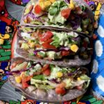 3 beautiful and brightly colored Beyond meat tacos in blue corn tortilla shells with pico de gallo, avocado lime crema, pineapple salsa, tomato salsa, lettuce and cilantro
