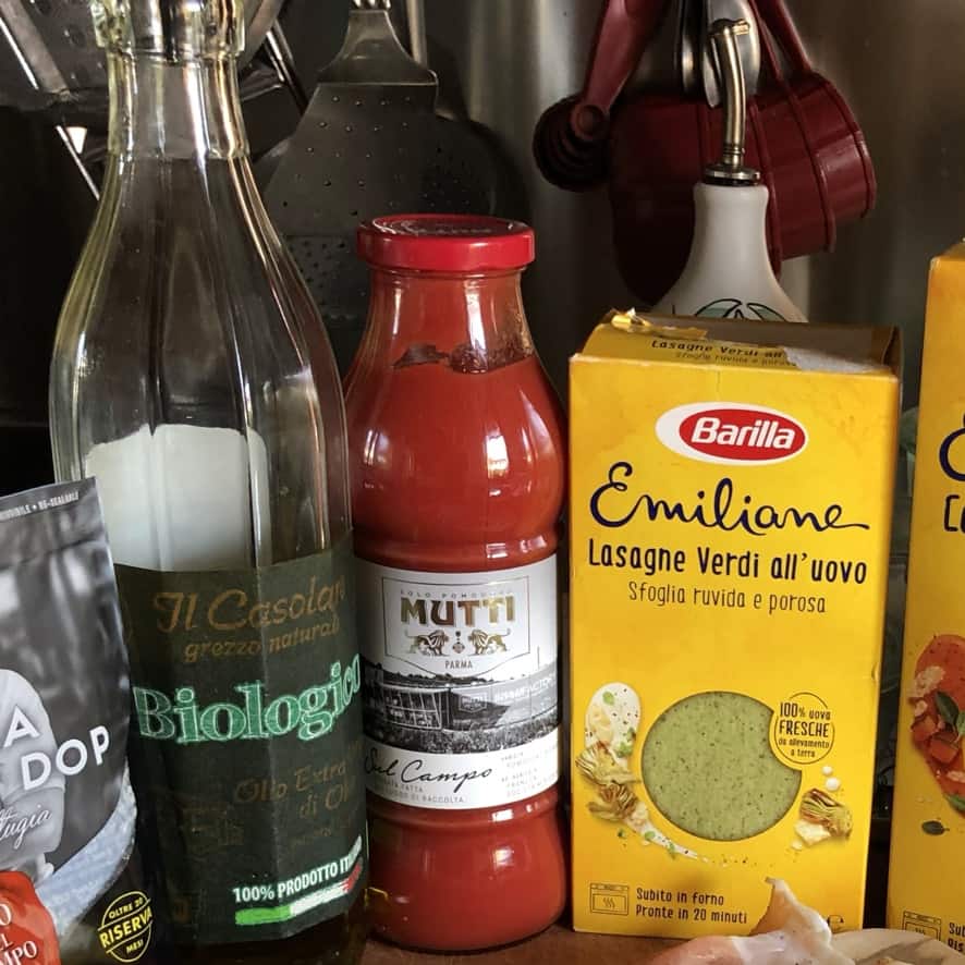 a jar of Mutti special edition Sul Campo tomato passata on the counter next to a bottle of organic extra virgin olive oil and spinach egg pasta lasagna noodles