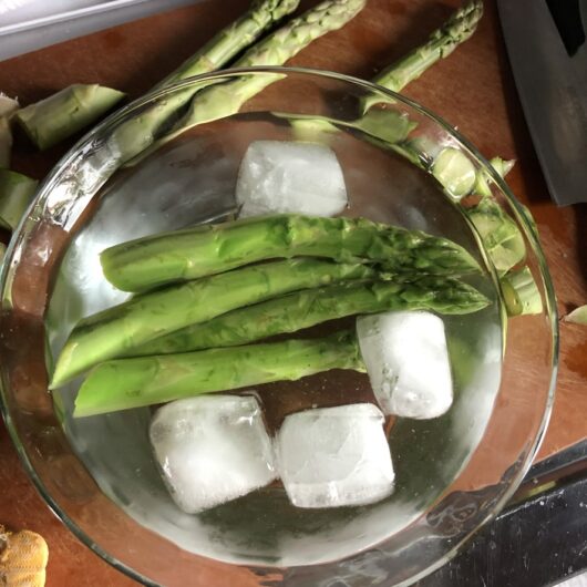 perfectly blanched asparagus spears (5 total) in a bowl of ice water