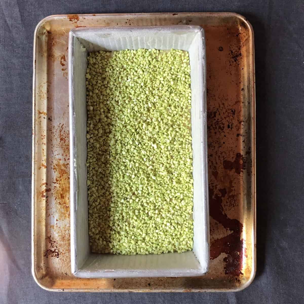 Banana bread batter in a loaf pan topped with a layer of freeze-dried pistachios ready to bake.
