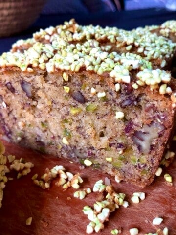 Sliced pistachio banana nut bread with freeze-dried pistachios on top and pistachios and pecans visible throughout the moist crumb.