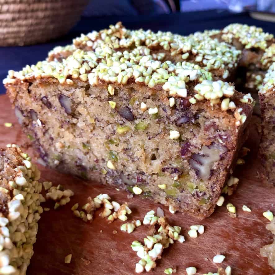 Sliced pistachio banana nut bread with freeze-dried pistachios on top and pistachios and pecans visible throughout the moist crumb.