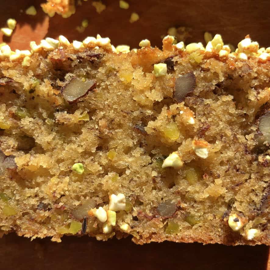 Extreme closeup of a slice of pistachio banana nut bread showing pistachios and pecans throughout the moist crumb.