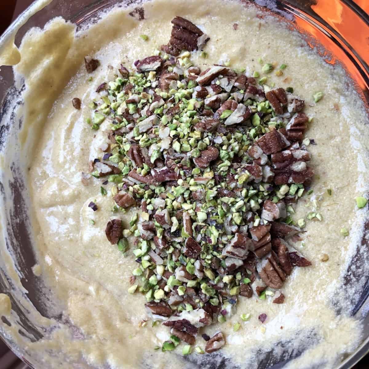 Chopped pistachios and pecans added to banana bread batter in a mixing bowl before folding in.
