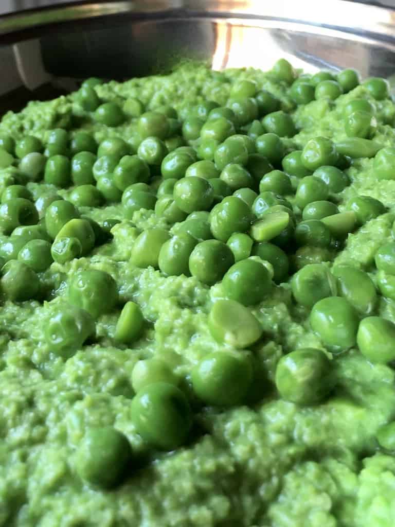 mushy peas with whole peas dolloped on top in an oval stainless steel serving dish