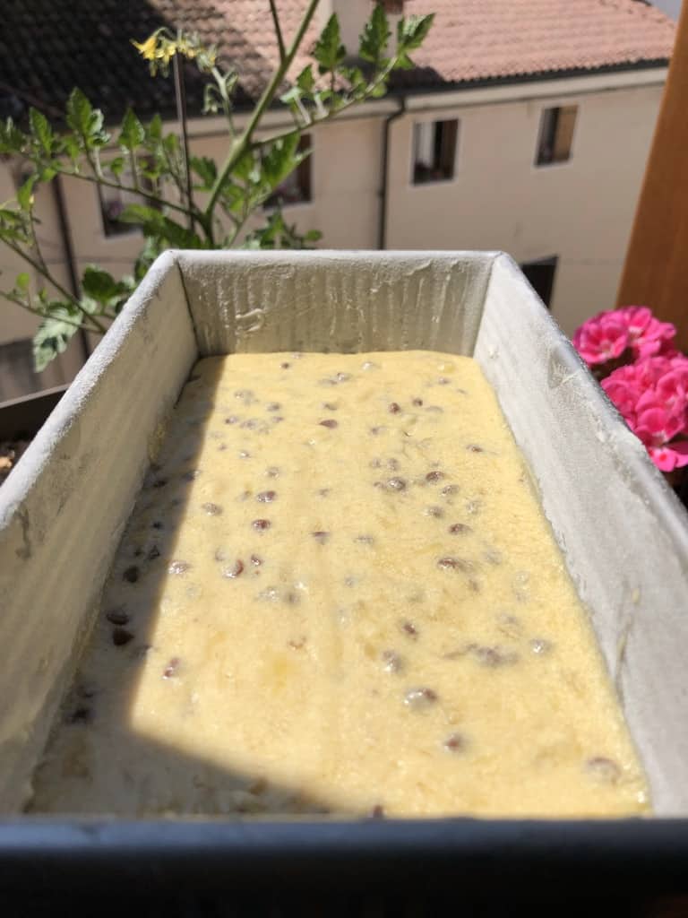 all of the mini chocolate chips mixed into the banana bread batter in a loaf pan with a view of bright pink gardenia flowers and Italian rooftops in the distance