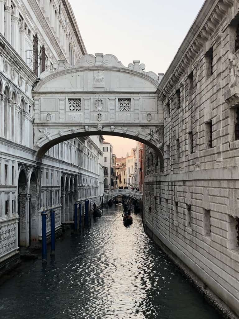 Venice canal with all white buildings on both sides connected by an ancient sky bridge
