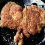 perfectly golden brown crispy Chicken cutlet frying in a cast iron skillet