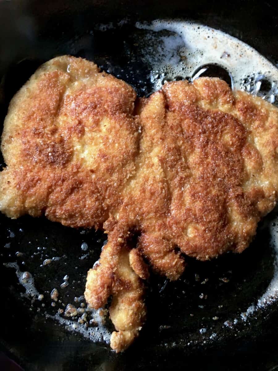 perfectly golden brown crispy Chicken cutlet frying in a cast iron skillet